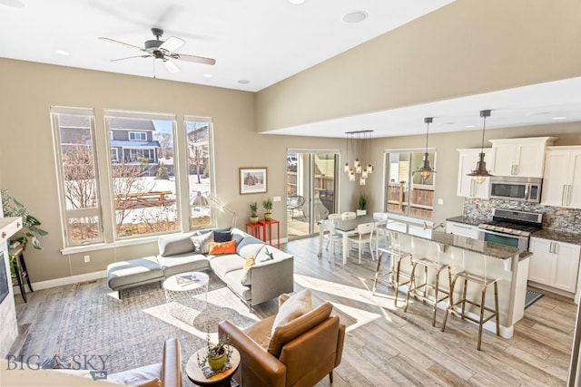 living area with baseboards, a healthy amount of sunlight, a ceiling fan, and light wood finished floors