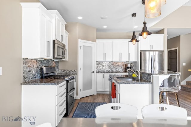 kitchen featuring a breakfast bar, a kitchen island with sink, a sink, stainless steel appliances, and white cabinets