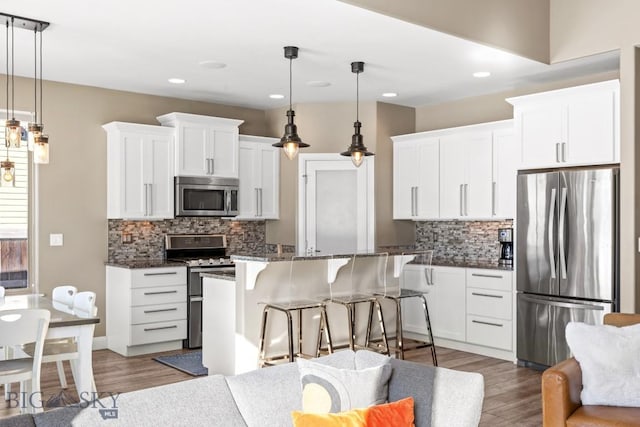 kitchen featuring dark stone countertops, wood finished floors, stainless steel appliances, white cabinets, and a kitchen breakfast bar