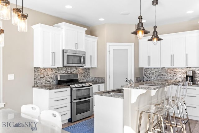 kitchen with dark stone counters, a sink, appliances with stainless steel finishes, white cabinetry, and a kitchen breakfast bar