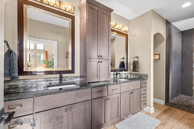 full bathroom featuring double vanity, a tile shower, wood finished floors, and a sink