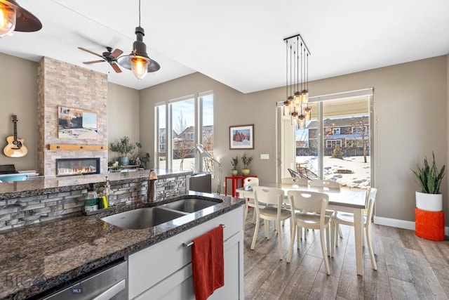 kitchen with a sink, stainless steel dishwasher, dark stone counters, a large fireplace, and light wood finished floors