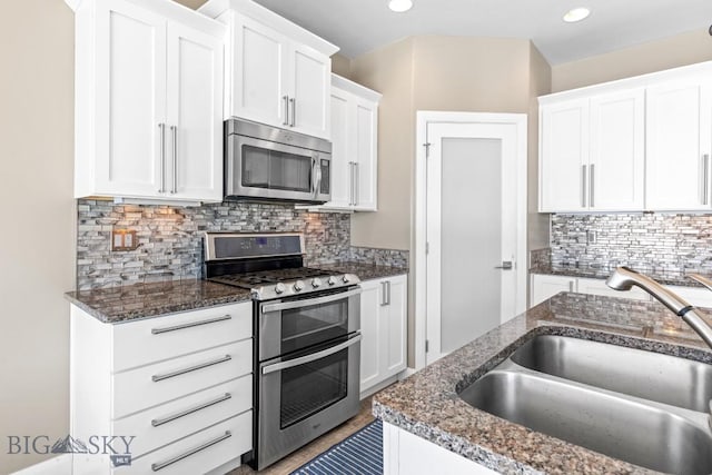 kitchen featuring backsplash, dark stone counters, appliances with stainless steel finishes, white cabinetry, and a sink