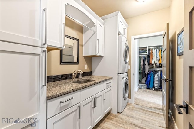 laundry room featuring stacked washer and dryer, light wood-style flooring, a sink, cabinet space, and baseboards