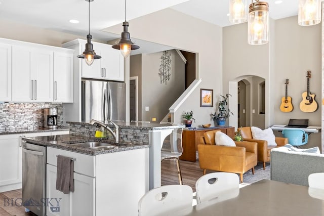 kitchen with a center island with sink, a sink, backsplash, stainless steel appliances, and arched walkways