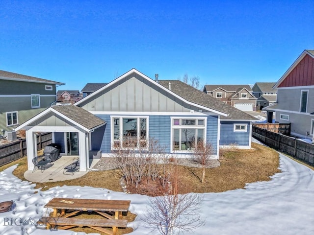 snow covered property featuring a patio, board and batten siding, a shingled roof, and fence