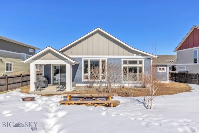 snow covered back of property featuring a fire pit, board and batten siding, and fence