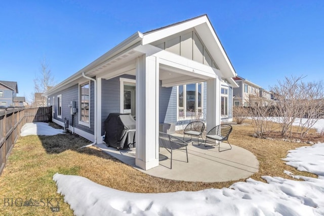 snow covered property with a patio area, board and batten siding, and fence