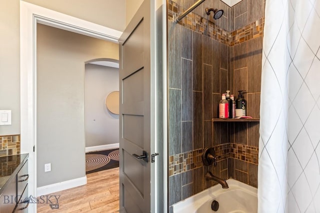 bathroom featuring wood finished floors, shower / bathtub combination with curtain, and baseboards