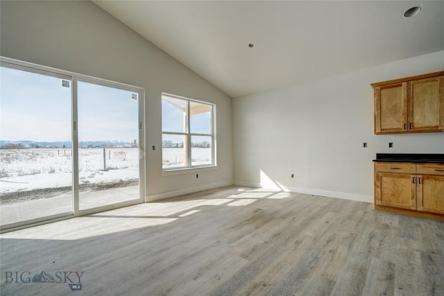 unfurnished living room with baseboards, lofted ceiling, and light wood-style floors