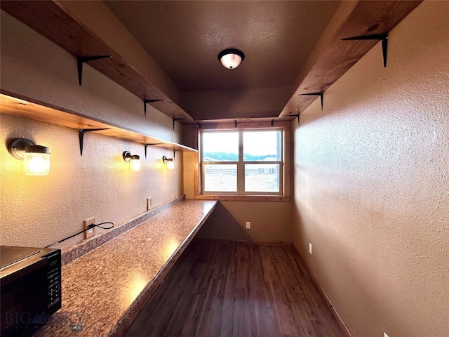 bar featuring baseboards, dark wood-type flooring, black microwave, and a textured wall