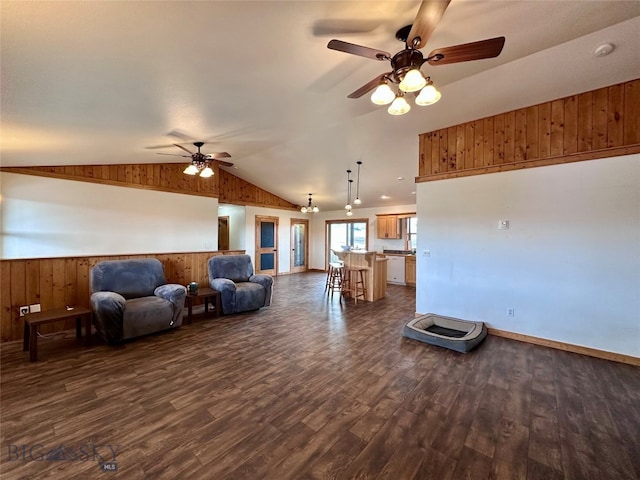 living area with wood walls, vaulted ceiling, wainscoting, a ceiling fan, and dark wood-style flooring