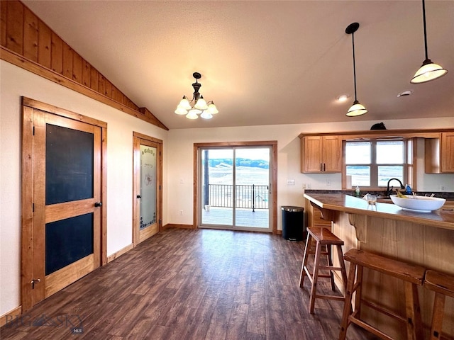 kitchen with brown cabinets, a breakfast bar, dark wood finished floors, vaulted ceiling, and hanging light fixtures