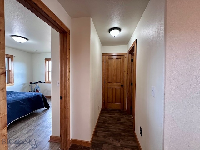 hallway with a textured ceiling, baseboards, and wood finished floors