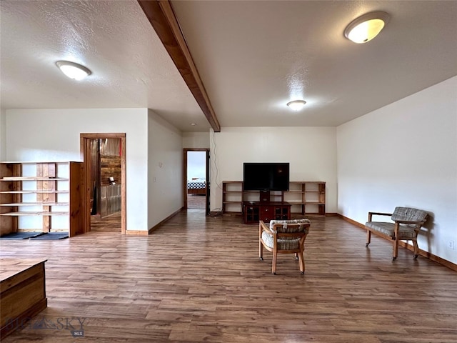 living area featuring beamed ceiling, a textured ceiling, baseboards, and wood finished floors