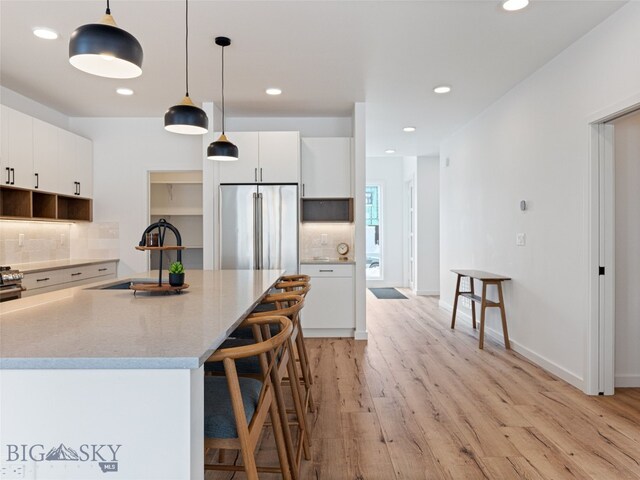 2824 S 30th Ave, Bozeman, MT 59718 - kitchen with a sink, decorative backsplash, light wood-type flooring, a breakfast bar area, and white cabinetry