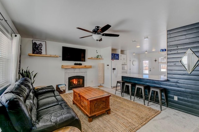 living room with rustic walls, carpet, a ceiling fan, and a tile fireplace