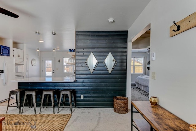 kitchen featuring a kitchen bar, rustic walls, white appliances, white cabinetry, and a ceiling fan