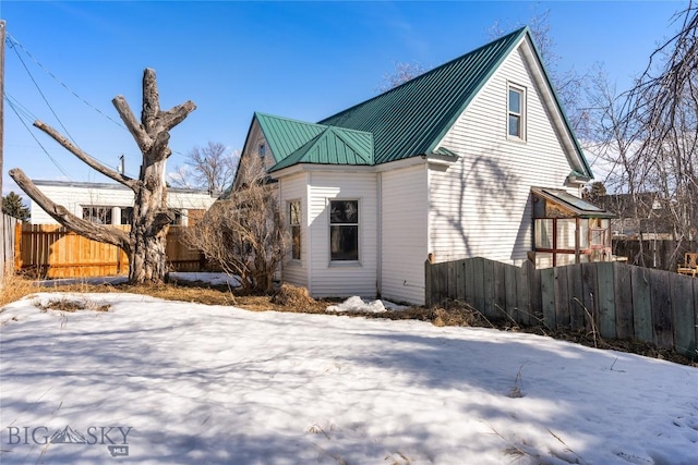 snow covered rear of property featuring metal roof and fence