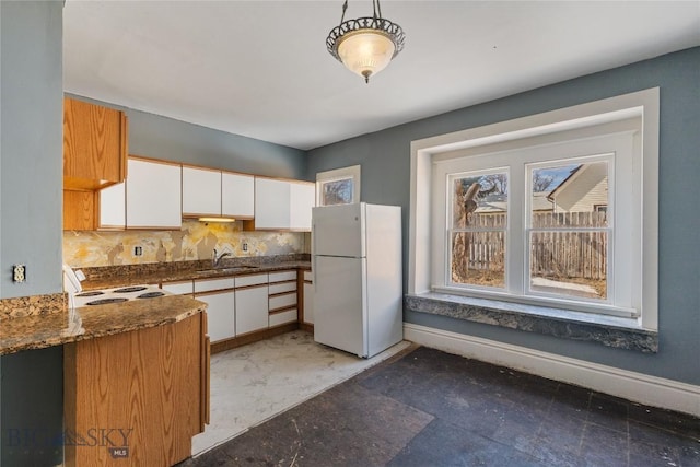 kitchen with white appliances, baseboards, dark stone counters, a sink, and white cabinets