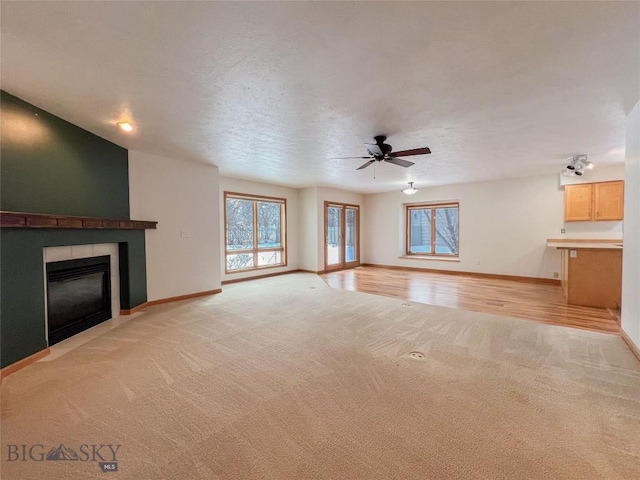 unfurnished living room with a tiled fireplace, light colored carpet, baseboards, and a ceiling fan