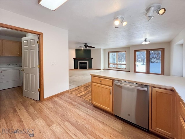 kitchen featuring light wood finished floors, dishwasher, washer / dryer, a fireplace, and a ceiling fan