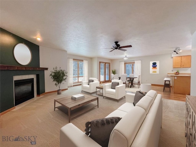 living area with a fireplace with flush hearth, light carpet, a textured ceiling, baseboards, and ceiling fan