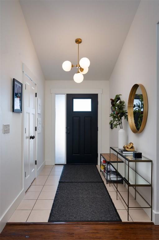 foyer featuring light tile patterned floors, a notable chandelier, baseboards, and lofted ceiling