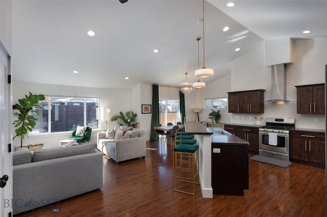 kitchen featuring stainless steel range with gas stovetop, open floor plan, a kitchen bar, wall chimney exhaust hood, and a sink