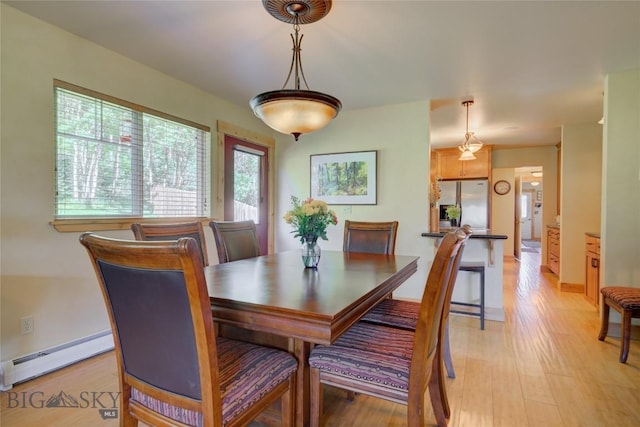 dining room featuring a baseboard heating unit, baseboards, and light wood-style floors