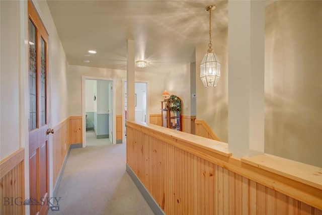 hallway featuring an upstairs landing, a wainscoted wall, and light colored carpet