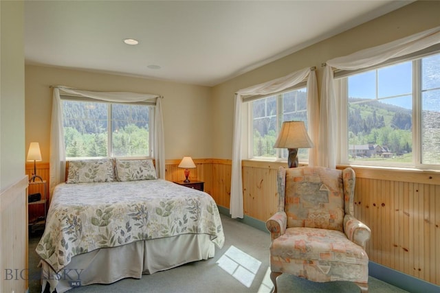 carpeted bedroom with multiple windows, wooden walls, and wainscoting