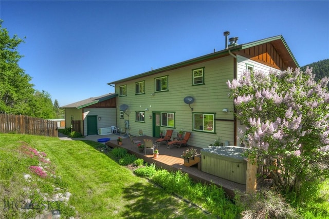 back of house with board and batten siding, a hot tub, fence, a wooden deck, and a lawn