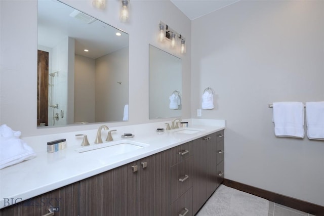 bathroom featuring double vanity, a stall shower, baseboards, and a sink