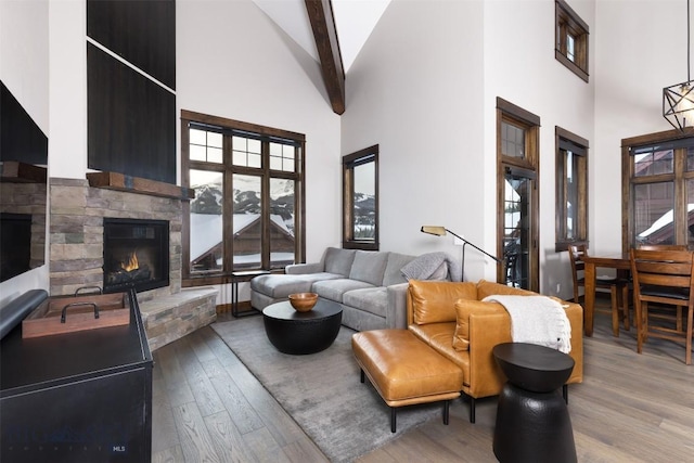 living room with a stone fireplace, beamed ceiling, wood finished floors, and high vaulted ceiling