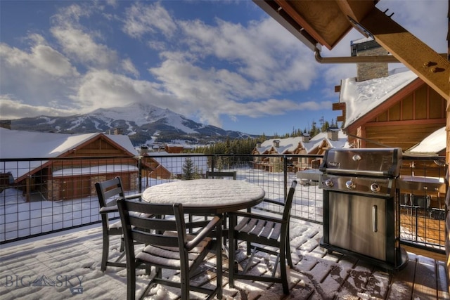 snow covered patio with a mountain view, a balcony, and a grill