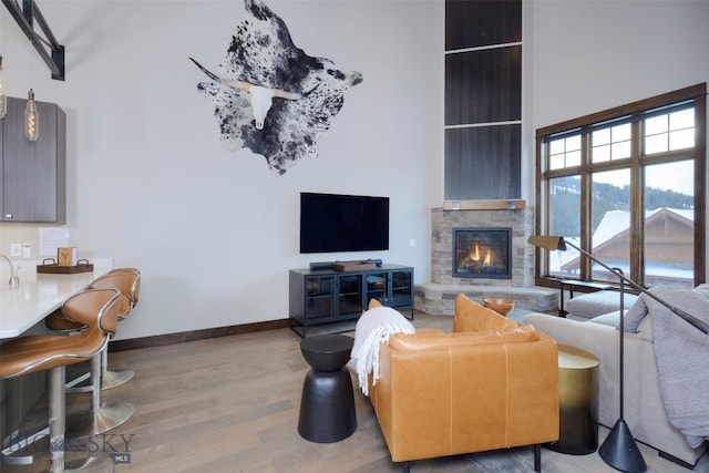 living room featuring a stone fireplace, a high ceiling, baseboards, and wood finished floors