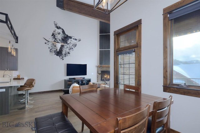 dining room featuring a notable chandelier, a warm lit fireplace, baseboards, and wood finished floors