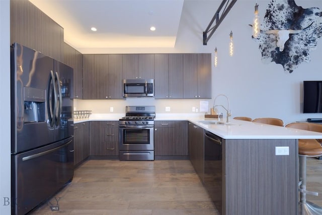 kitchen featuring a breakfast bar area, a peninsula, light wood-style flooring, a sink, and appliances with stainless steel finishes