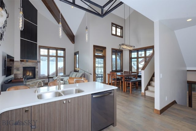 kitchen featuring open floor plan, light countertops, stainless steel dishwasher, a glass covered fireplace, and a sink