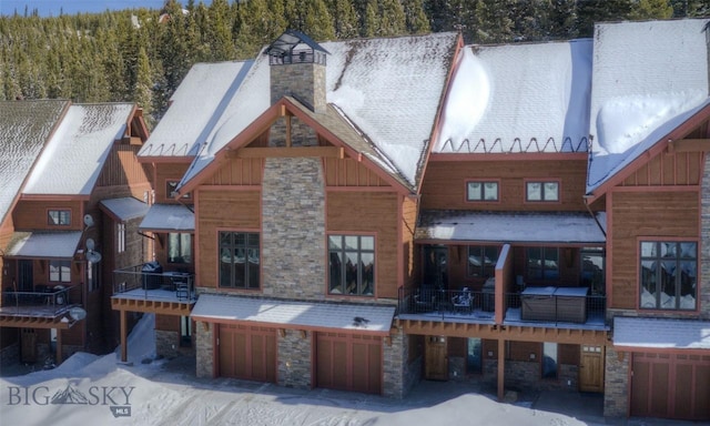 snow covered house with a garage, stone siding, and a chimney