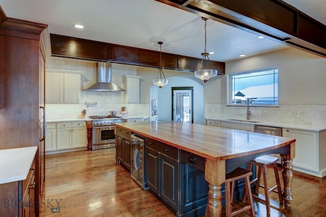 kitchen with light wood finished floors, beverage cooler, stainless steel appliances, wall chimney exhaust hood, and a sink