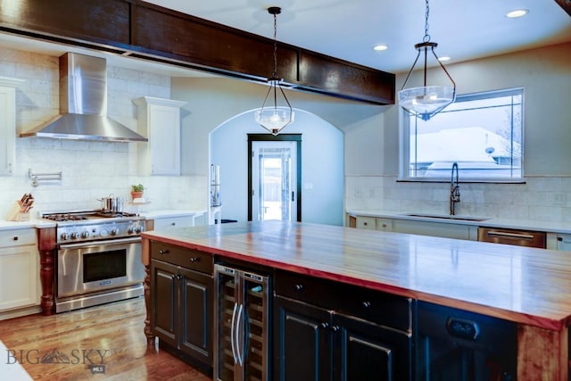 kitchen featuring beverage cooler, a sink, wood finished floors, stainless steel appliances, and wall chimney exhaust hood