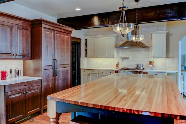 kitchen featuring decorative light fixtures, wall chimney exhaust hood, backsplash, and butcher block counters