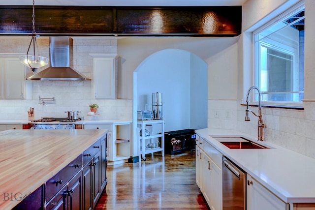 kitchen featuring dishwasher, light countertops, wall chimney range hood, and a sink