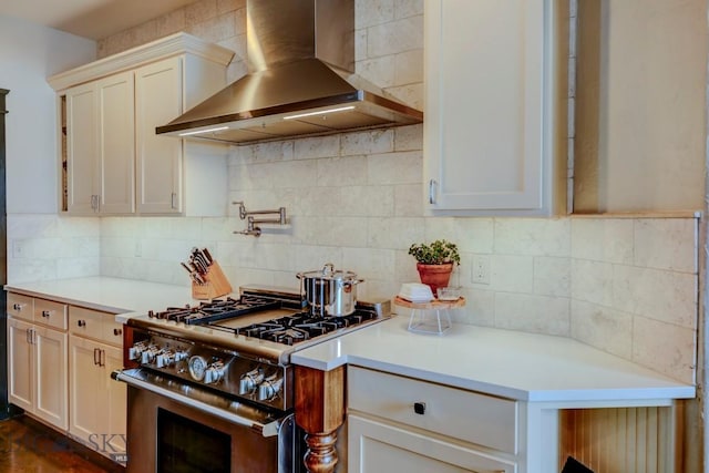 kitchen featuring light countertops, wall chimney exhaust hood, tasteful backsplash, and high end stove