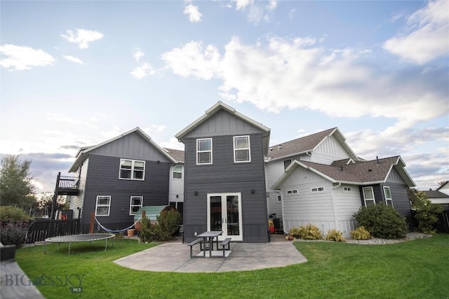 rear view of property featuring a lawn, a trampoline, french doors, board and batten siding, and a patio area