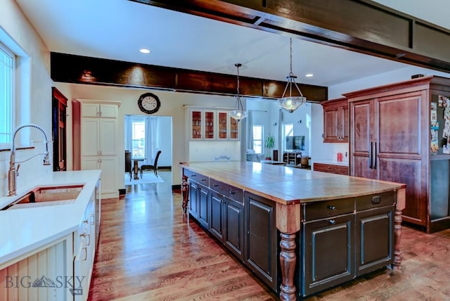 kitchen featuring wood finished floors, a sink, light countertops, a wealth of natural light, and a center island