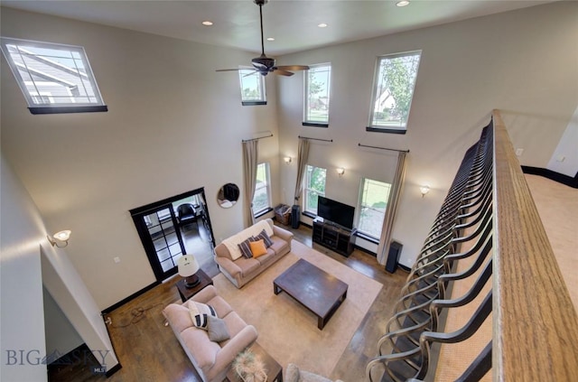 living area with wood finished floors, baseboards, recessed lighting, ceiling fan, and a towering ceiling