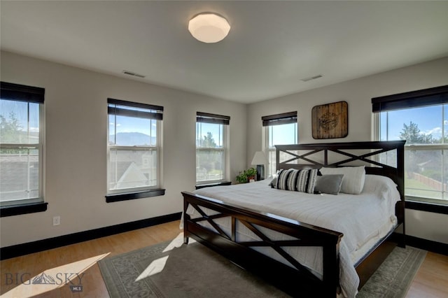 bedroom featuring multiple windows, light wood-style floors, visible vents, and baseboards